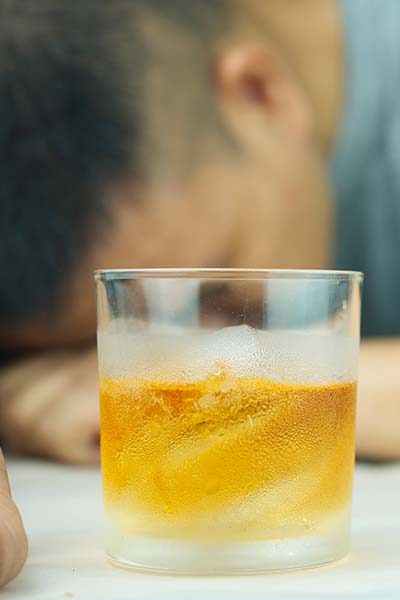 стакан с алкоголем крупным планом на фоне спящего мужчины